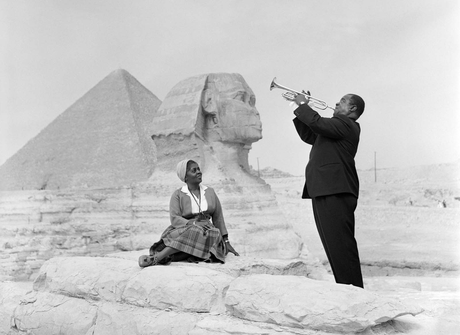 Американский джазовый музыкант Луи Армстронг играет на трубе на фоне Сфинкса, в то время как его жена сидит и слушает. 1961 год.