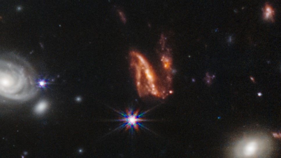 Эта извилистая оранжевая N-образная галактика, похоже, разрывается на части в результате галактического слияния