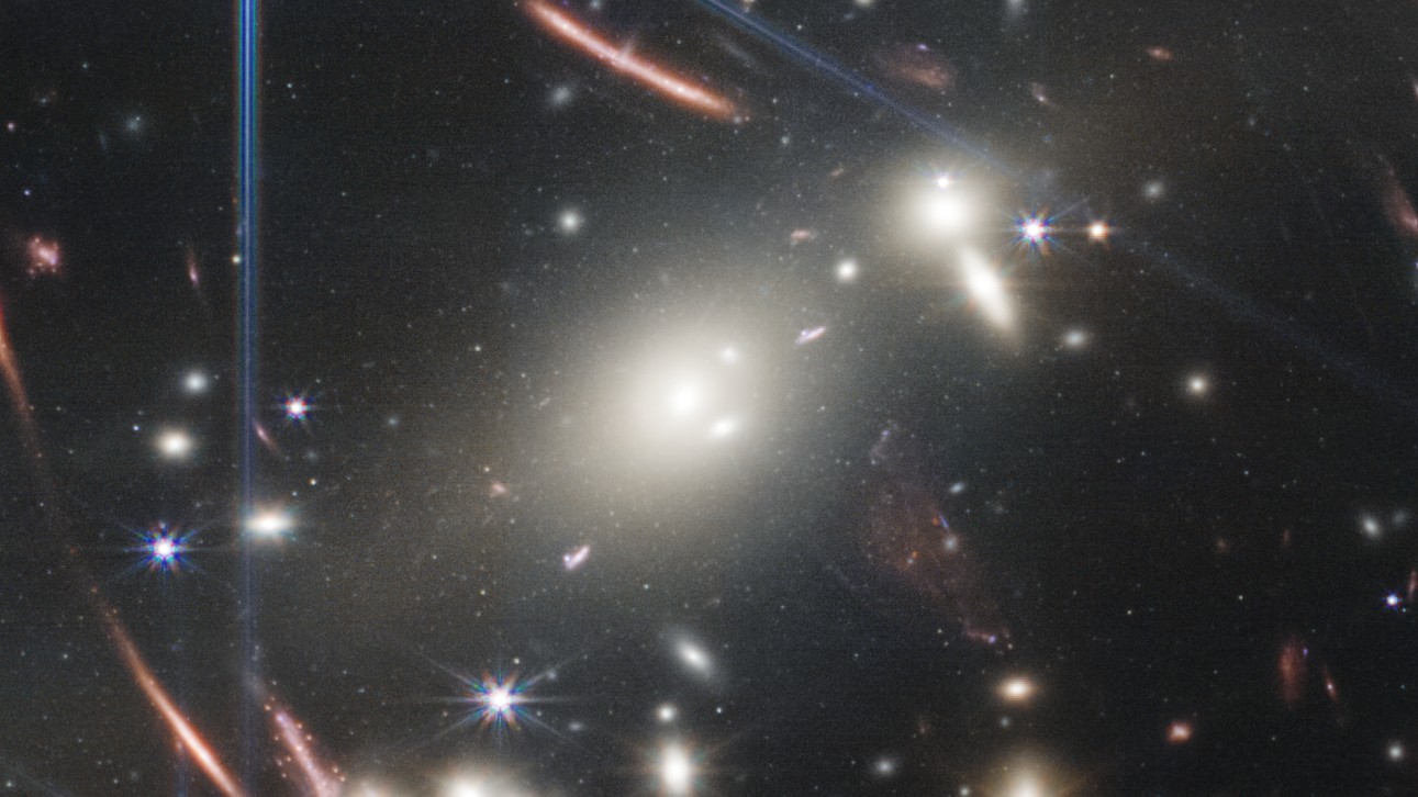 Огромное скопление галактик «извергает» дымку из белых звезд, когда несколько галактик сталкиваются в центре изображения JWST.